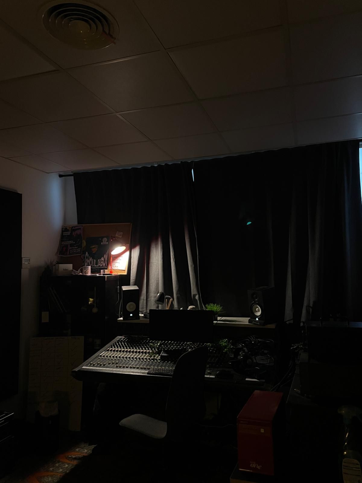 Sala de control del estudio en penumbra, con la mesa de mezclas iluminada por una lámpara