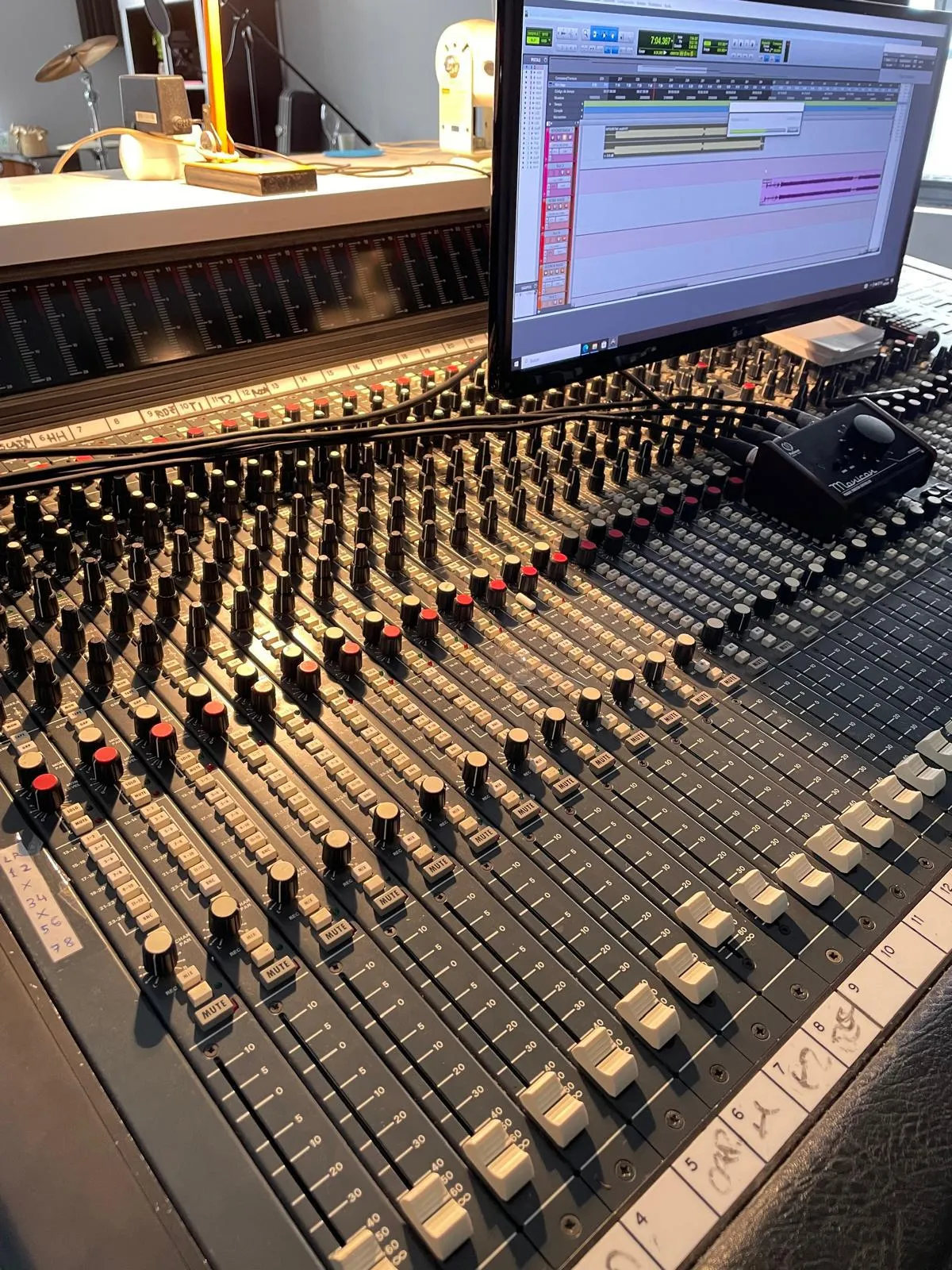 Mesa de mezclas analógica con faders y potenciómetros, junto a una pantalla con la sesión de grabación